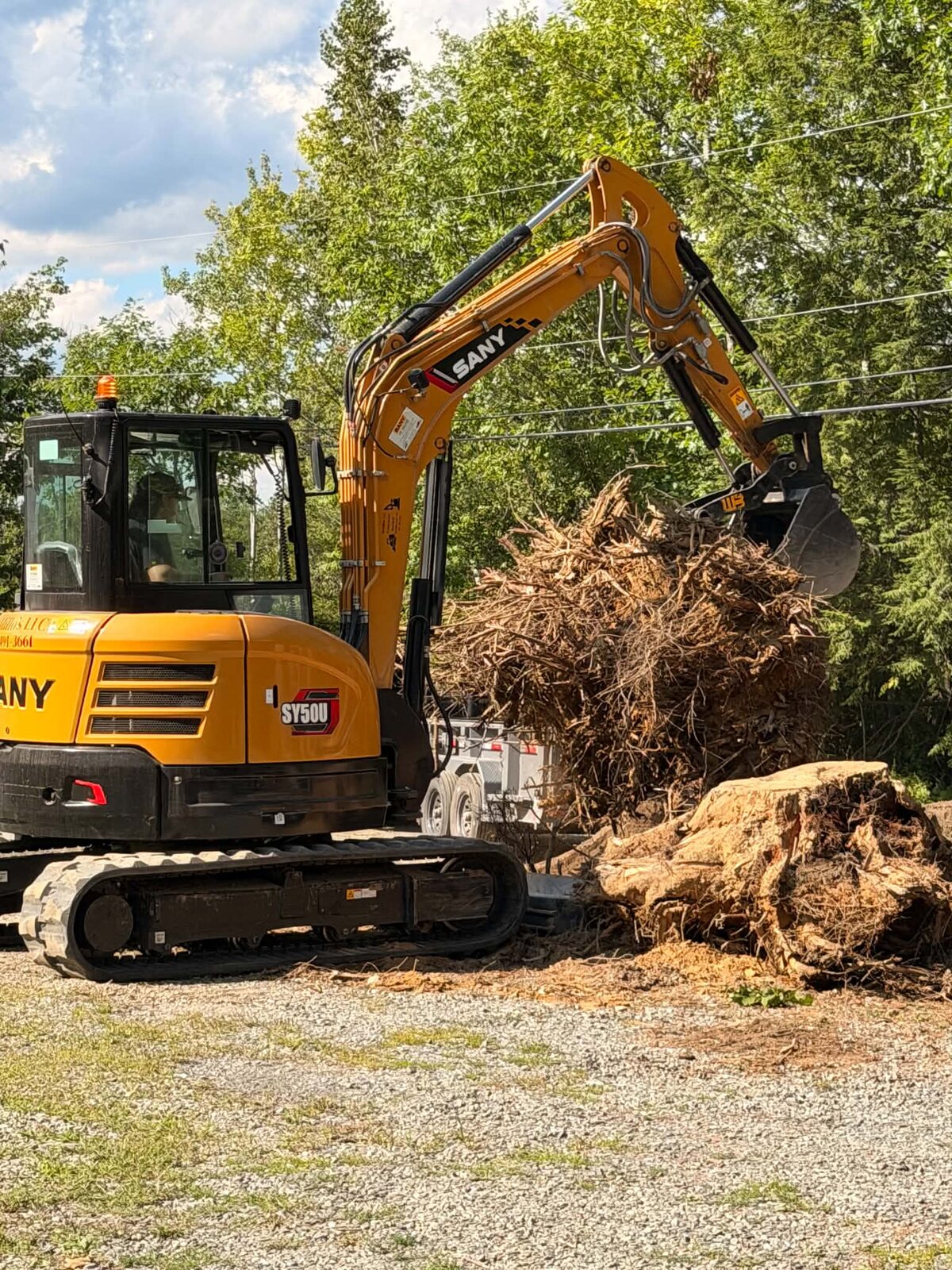 DeMillo's Excavation mini excavator loading a large tree stump and debris onto a trailer